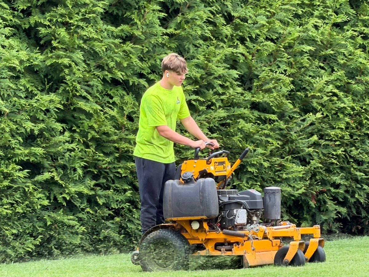 Gladiator crew member mowing along an arborvitae hedge