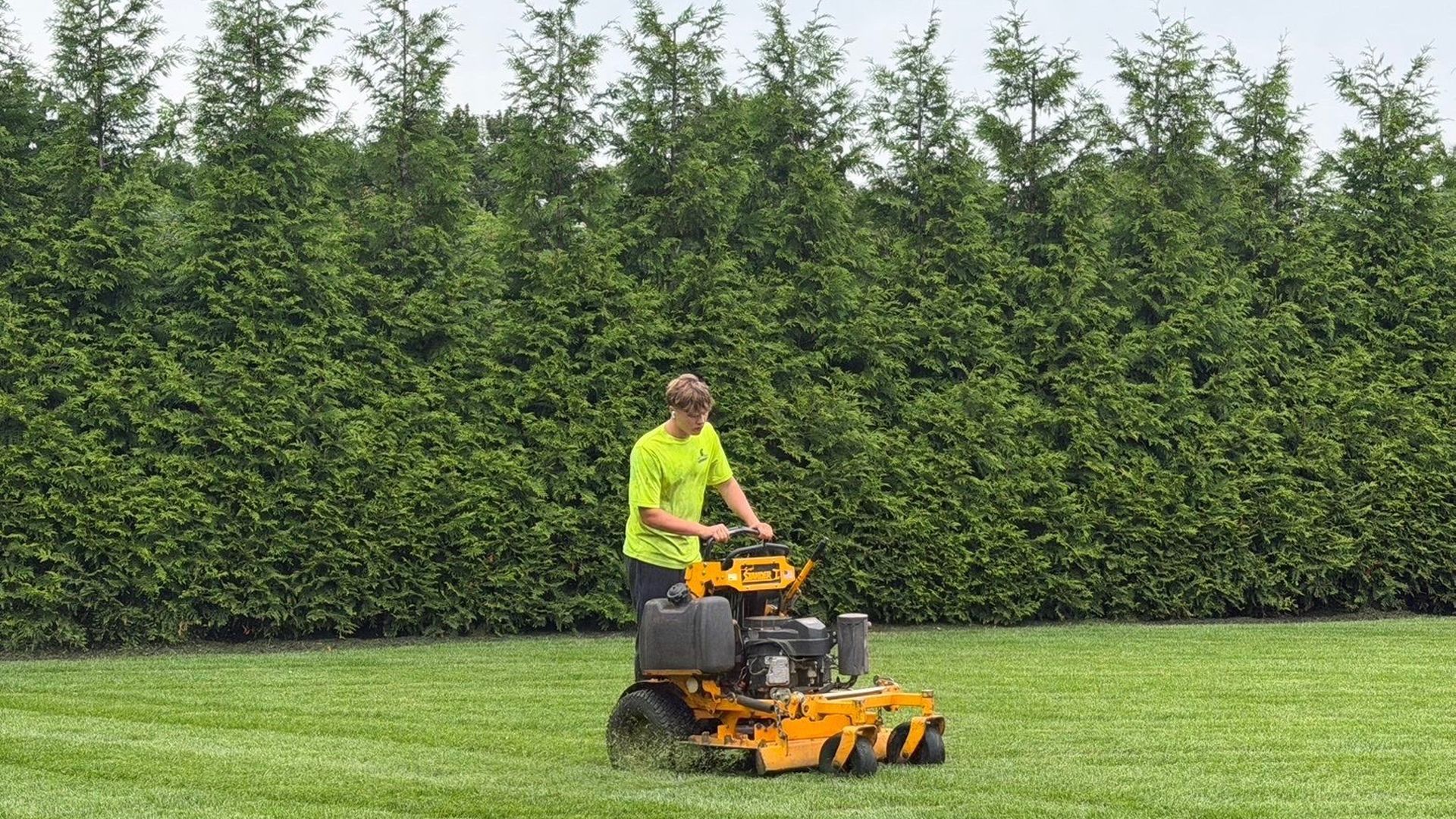 Gladiator crew mowing along a tall hedge on Long Island